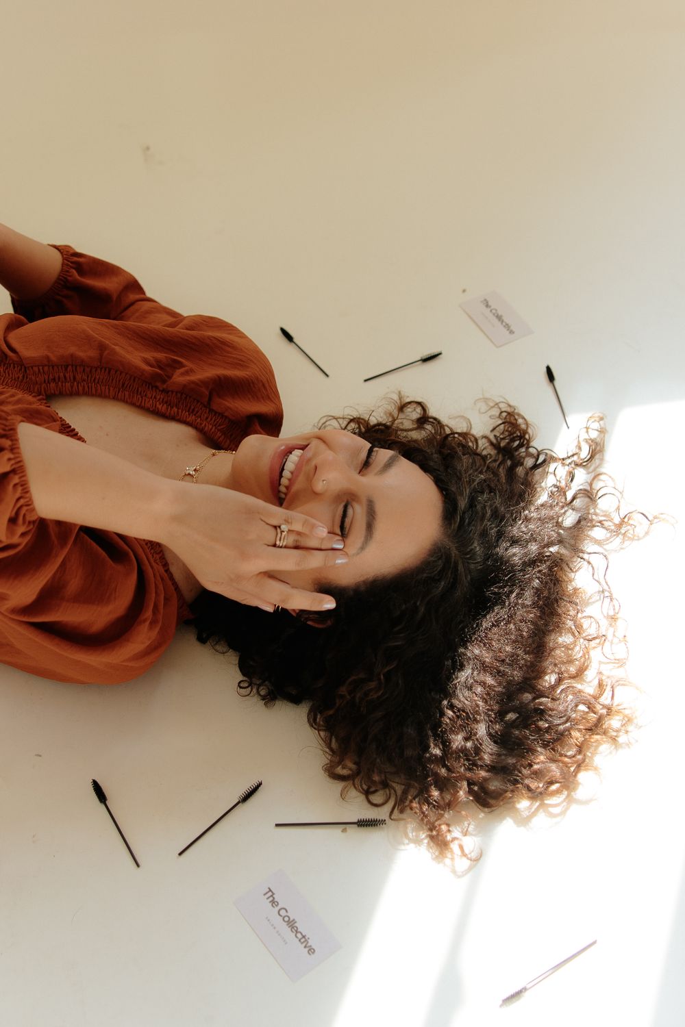 A person with curly hair wearing a rust colored top lying on a white background with scattered papers.