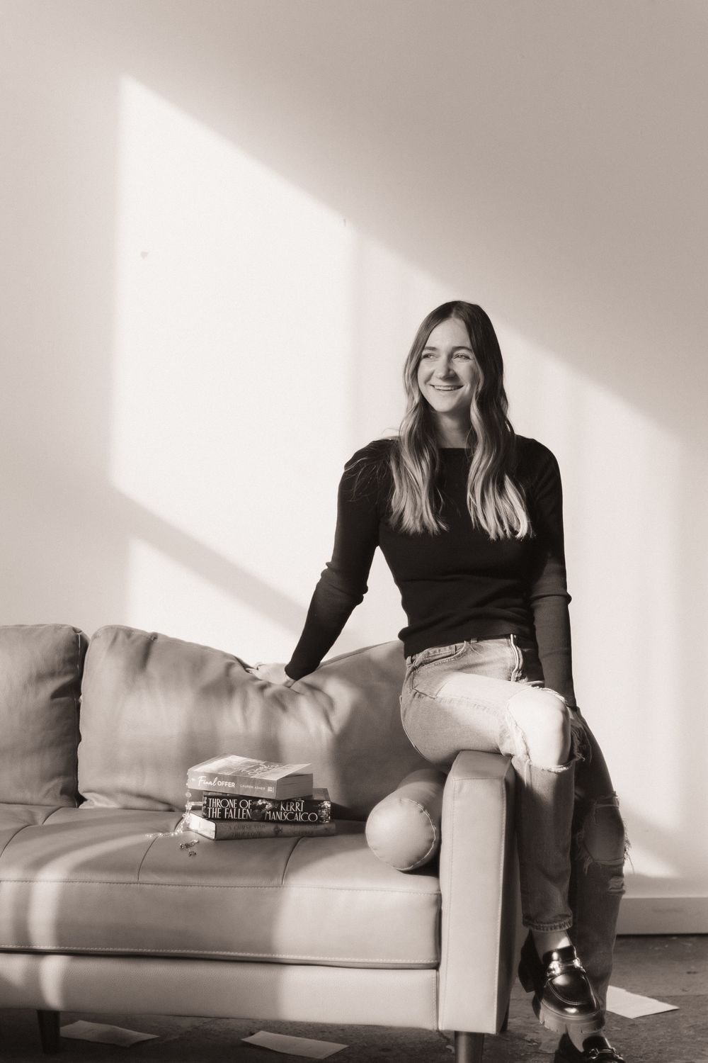 Black and white portrait of person sitting on leather couch in sunlit room with relaxed casual style.