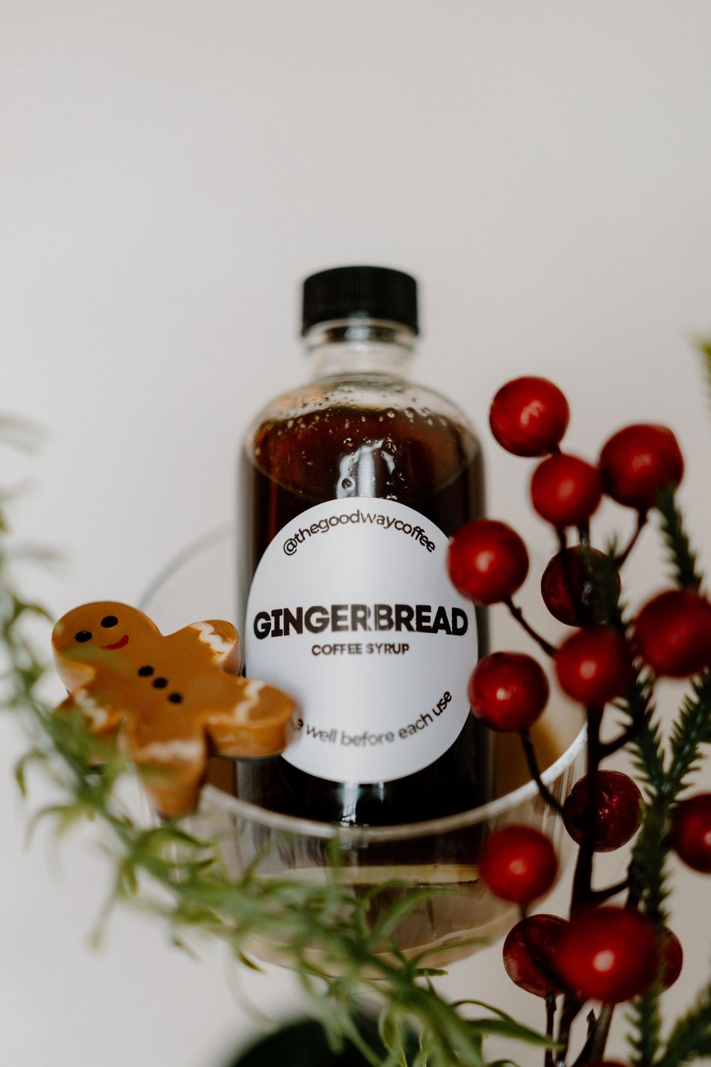 A bottle of gingerbread coffee syrup with festive red berries and gingerbread cookie decorations against a light background.