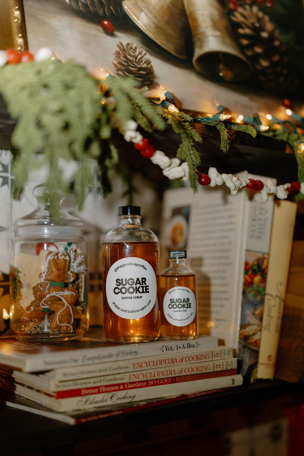 Glass bottles of bourbon and cocktail mixers arranged on a rustic wooden shelf with holiday decorations and pine cones.