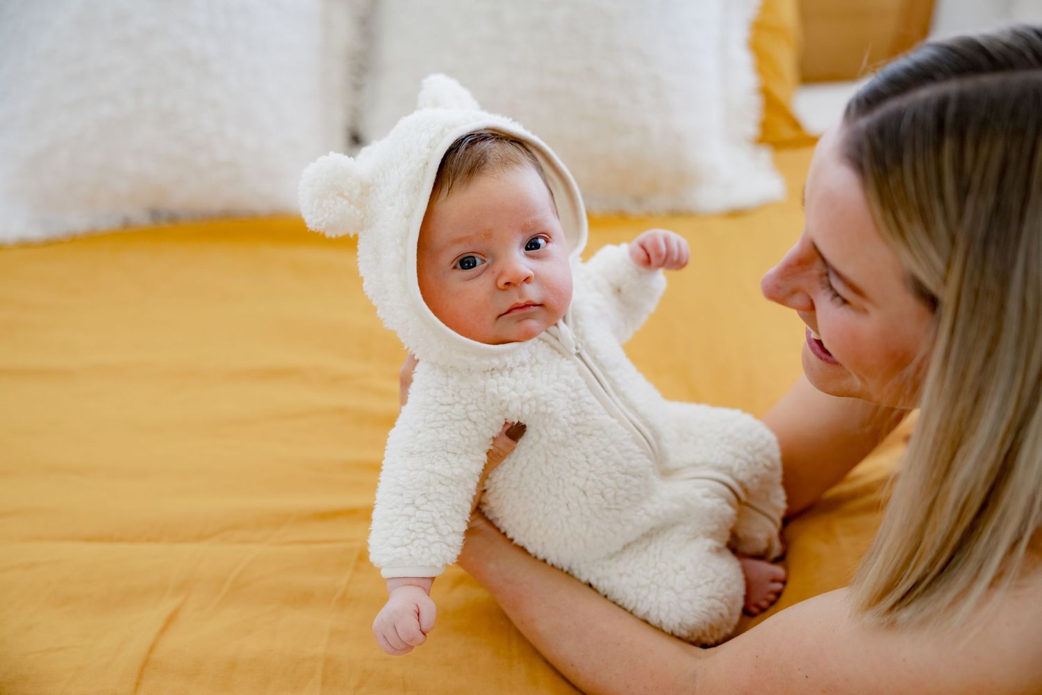 An infant wearing a soft white outfit being held on a yellow blanket.