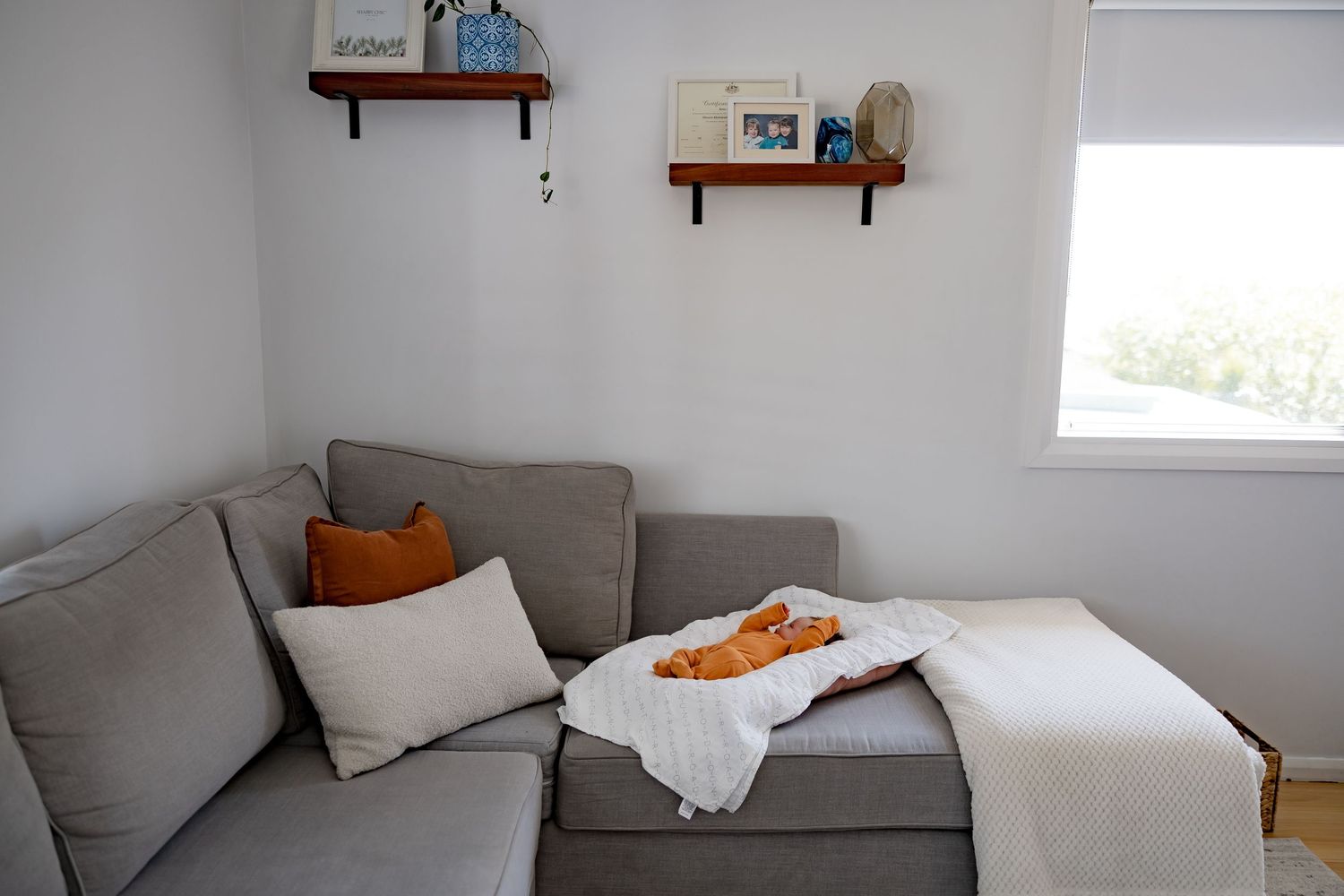 A modern living room with a gray sofa, orange accent pillows, and floating wooden shelves.
