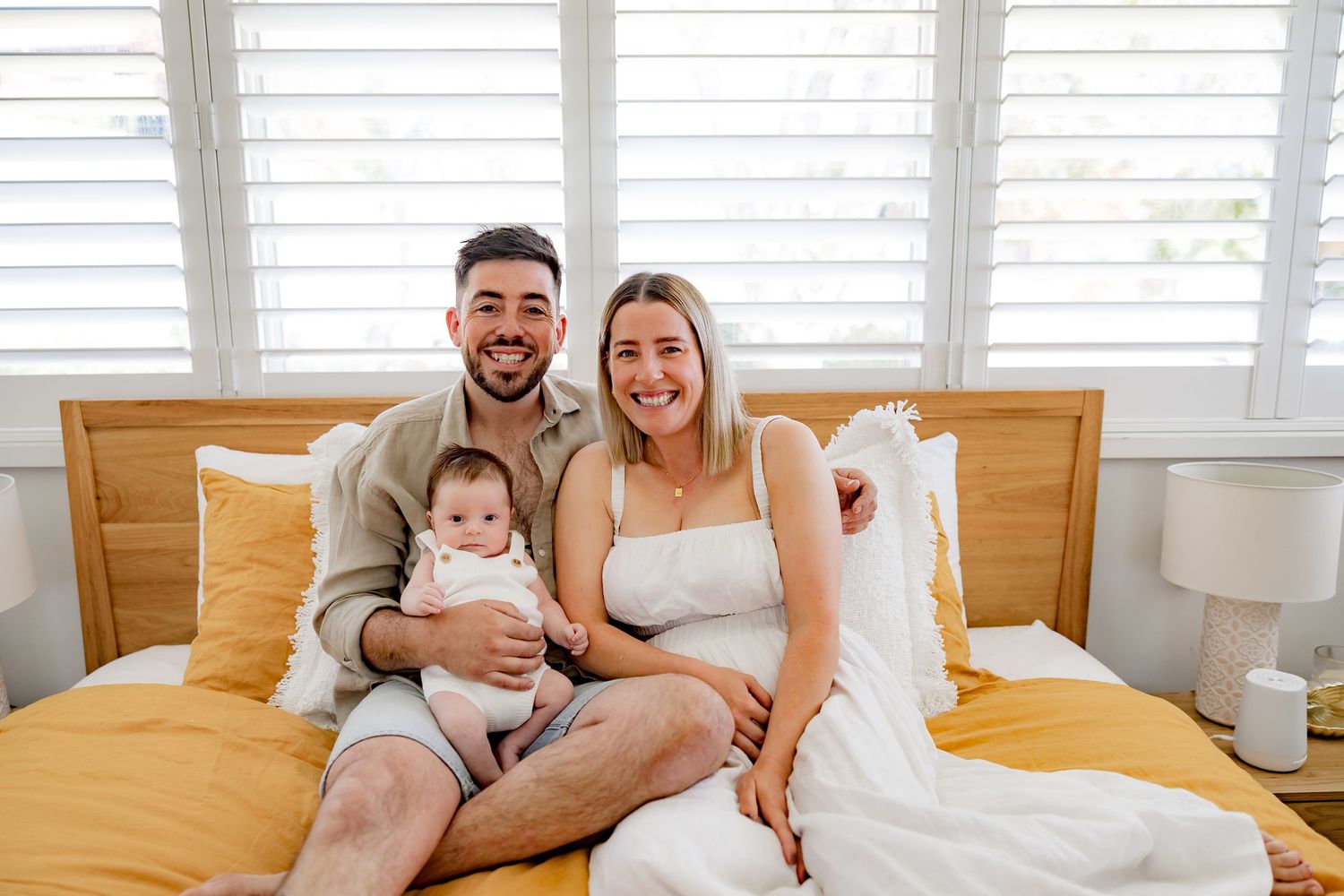 A family portrait on a bed with yellow bedding and wooden headboard.