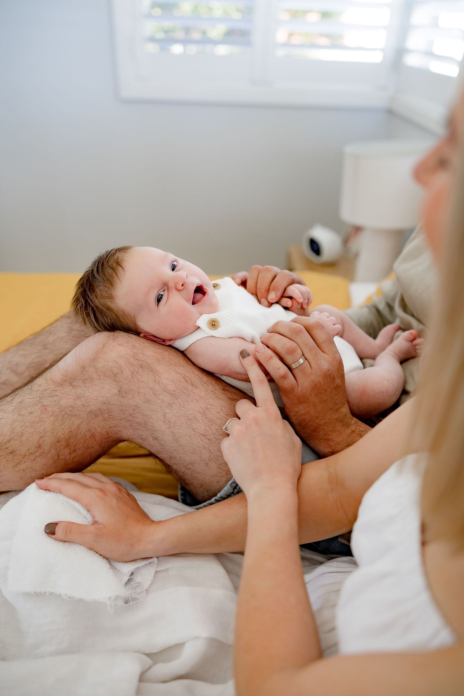 A baby lying on yellow bedding while being gently held.