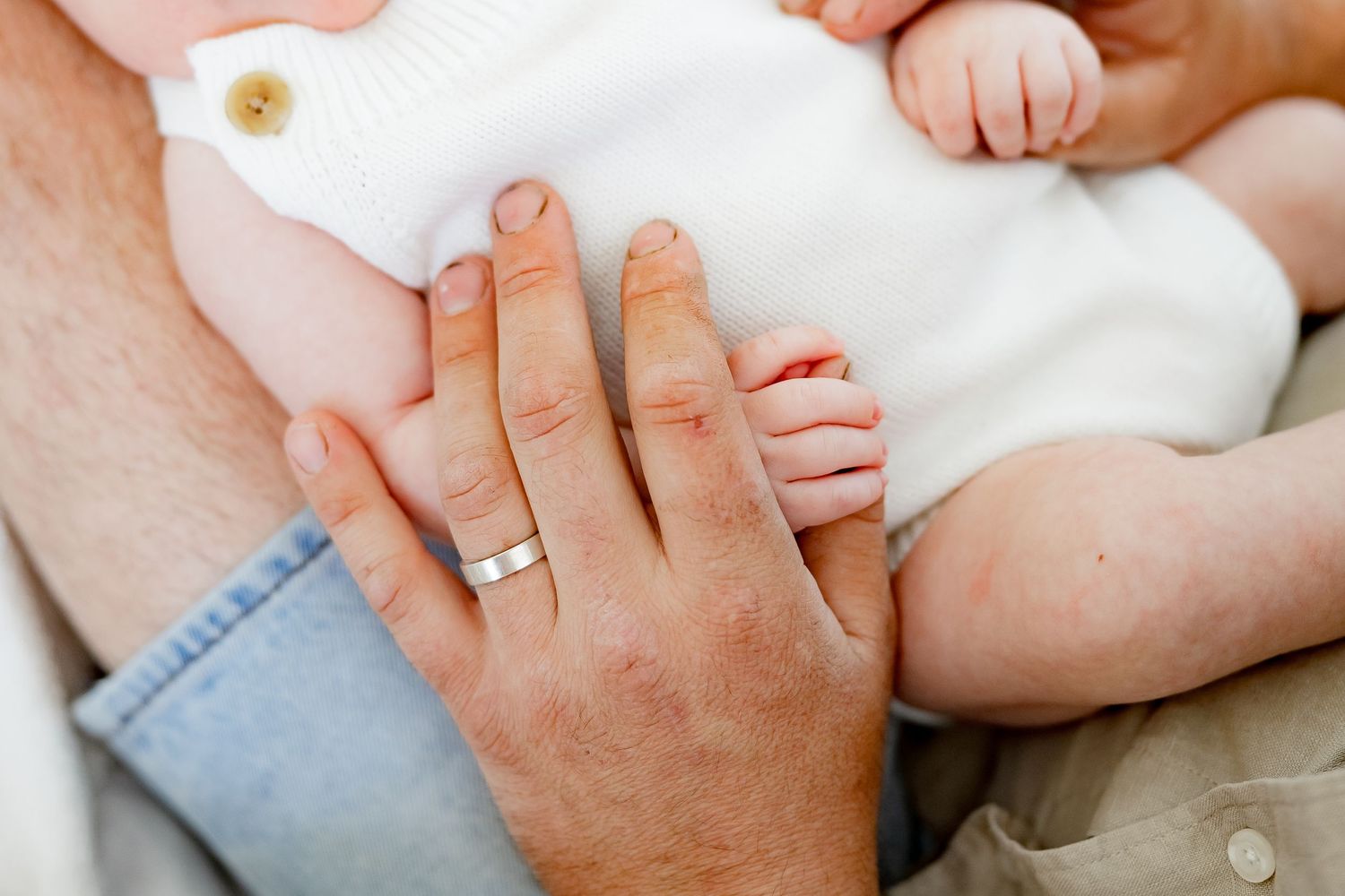 Close-up of hands tenderly touching a baby in white clothing.