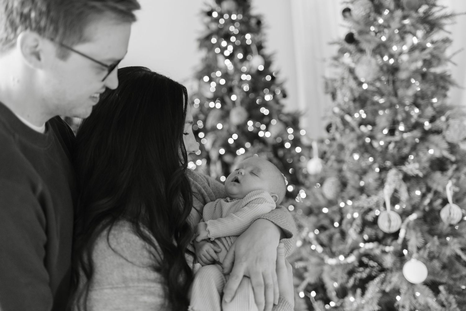 Family standing by Christmas tree holding newborn baby in black and white for a Toronto lifestyle newborn session, captured by Jess GC