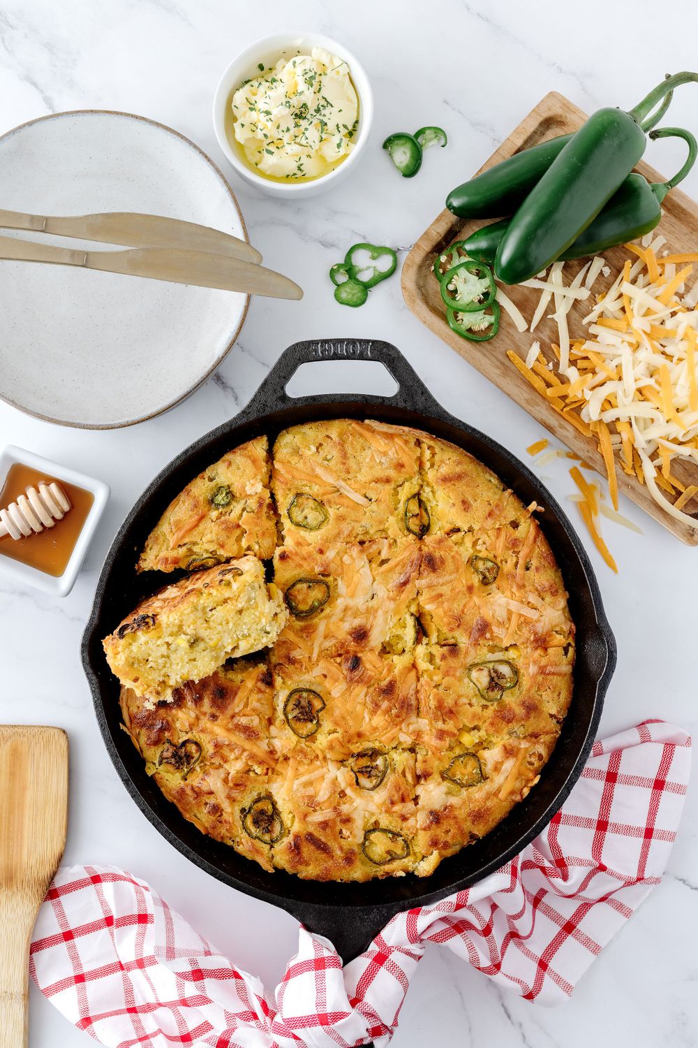 Jalapeno cornbread in cast iron skillet with honey and shredded cheese.