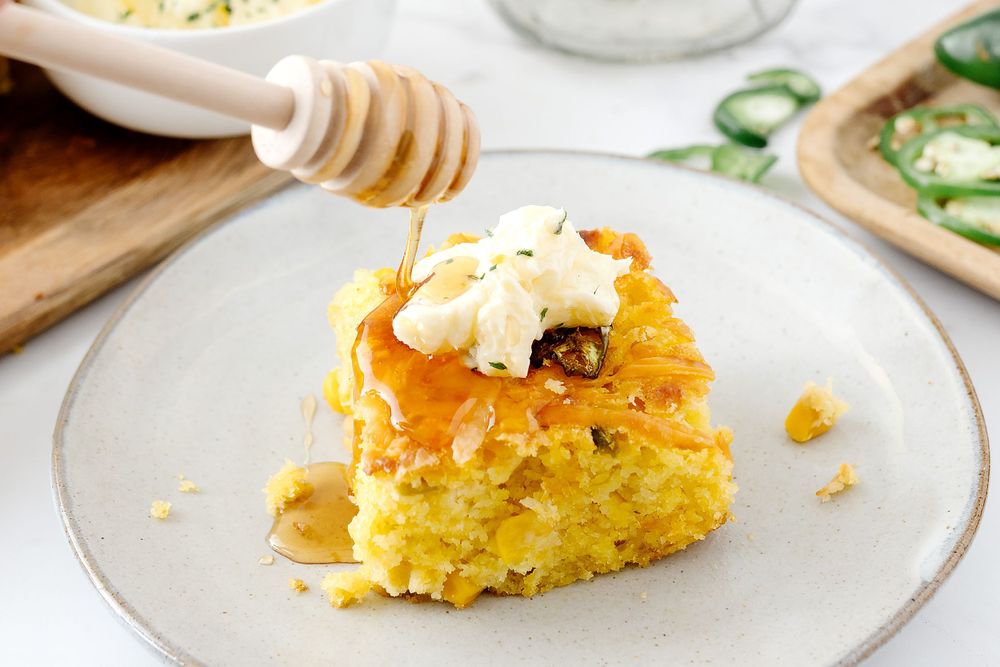 Slice of cornbread topped with honey and butter on a white plate.