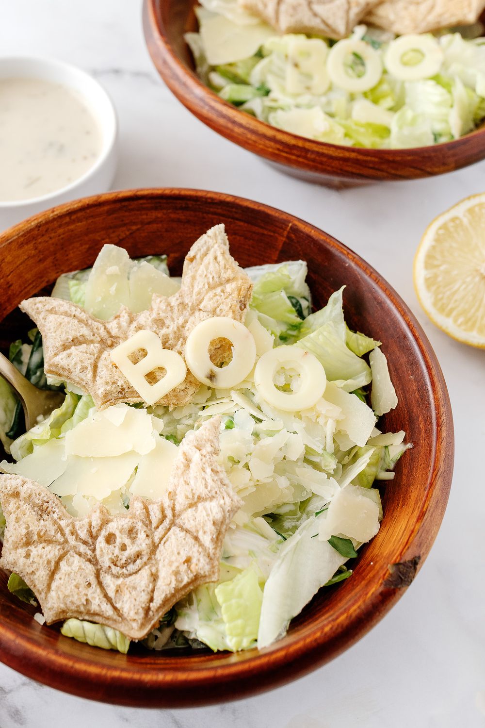 Caesar salad with sliced chicken, lettuce, and onion rings in wooden bowl.