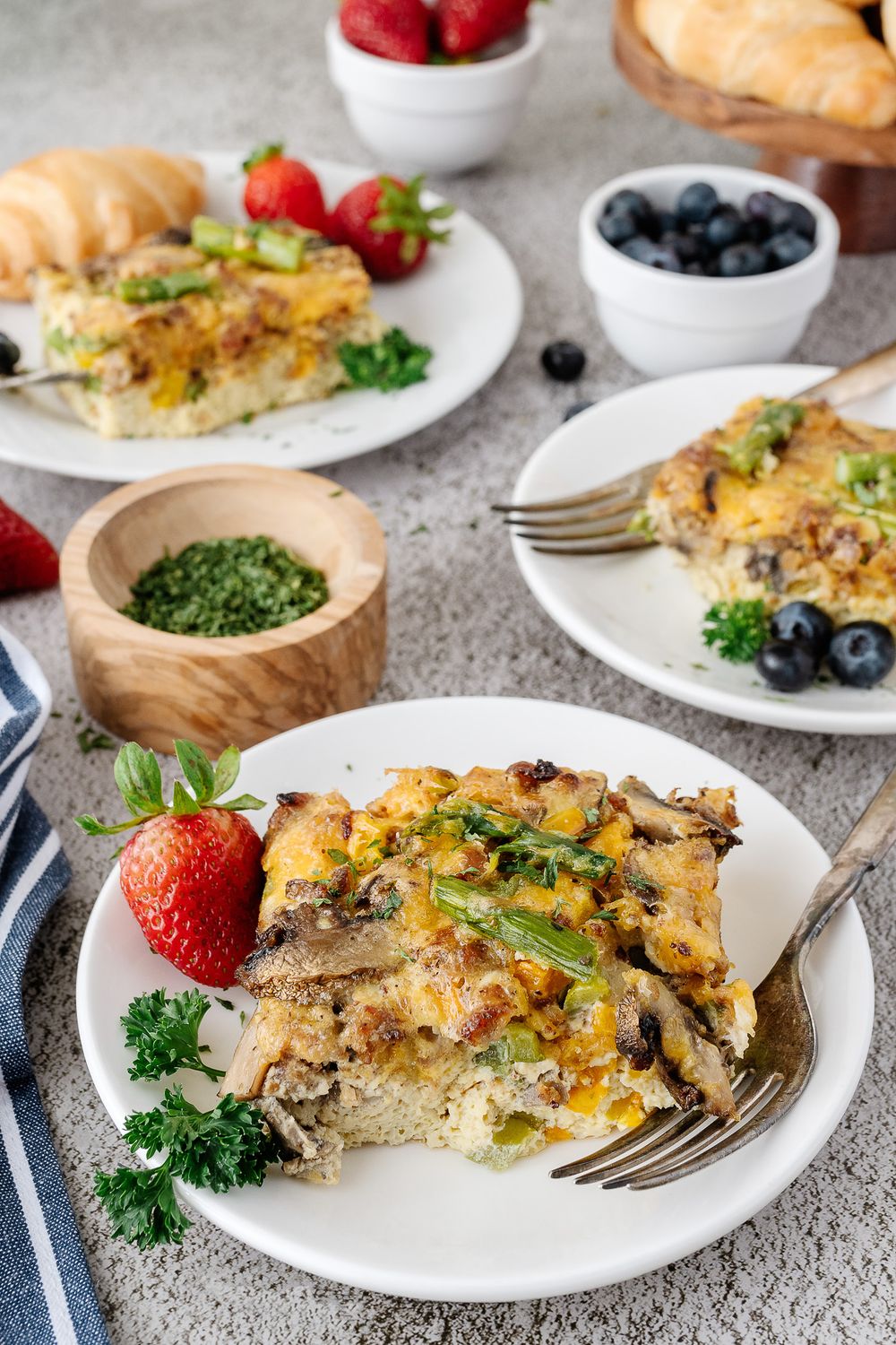 Breakfast casserole served with fresh berries and herbs on white plates.