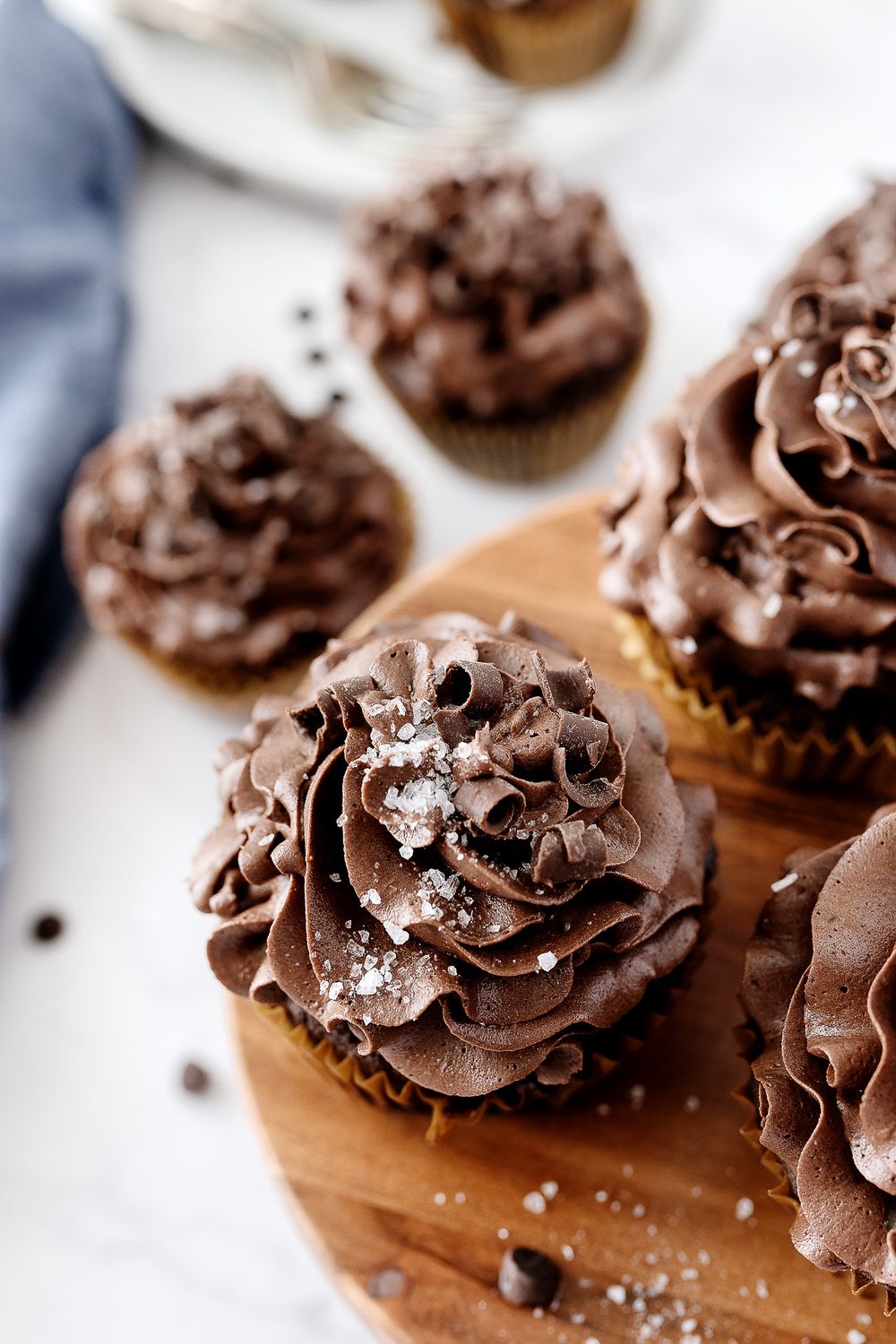 Chocolate cupcakes with swirled frosting and mini chocolate chips on wooden board.