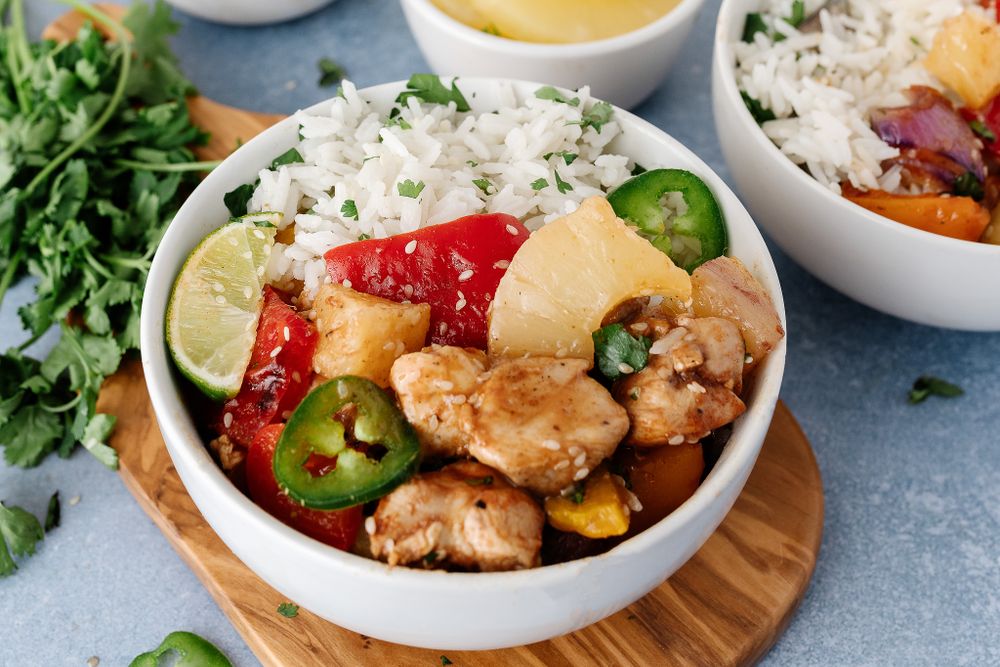 Bowl of rice with chicken, pineapple, jalapeños and red peppers served with lime wedges and fresh herbs.