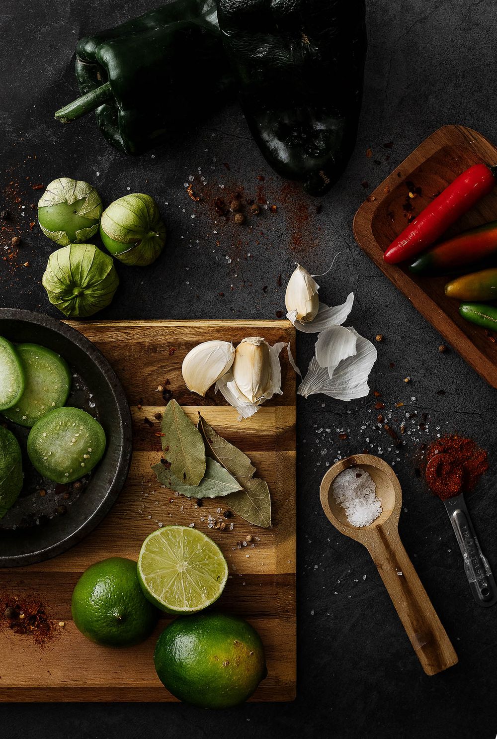 Fresh ingredients including limes, garlic, poblano peppers and spices arranged on a dark wooden cutting board.