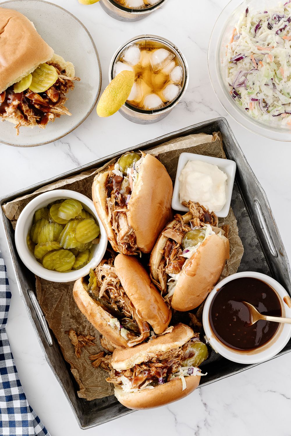 BBQ pulled pork sliders served with pickles, coleslaw and dipping sauce on a metal tray.