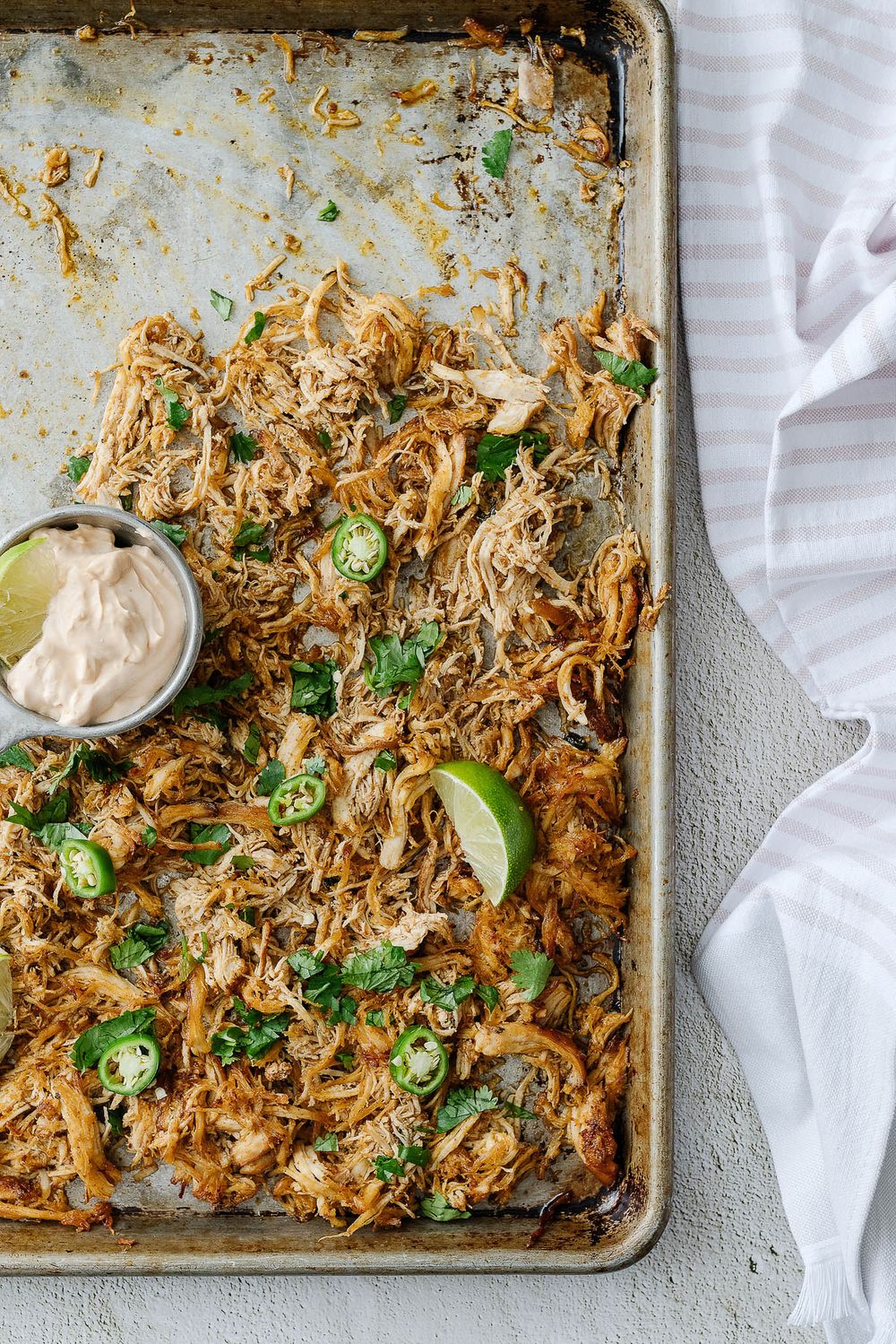 Shredded chicken with jalapeños and lime wedges on a sheet pan with garnishes.