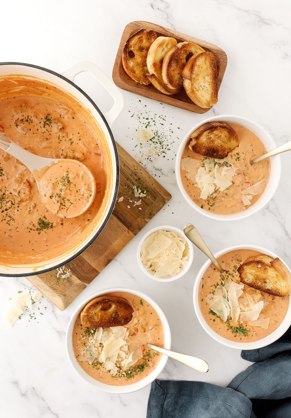 Creamy tomato soup served in white bowls with toasted bread and herbs on a marble countertop.