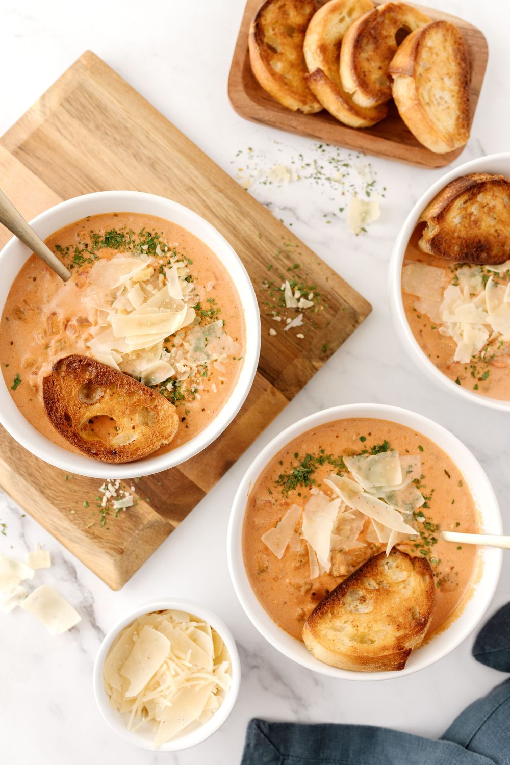 Bowls of creamy tomato soup garnished with melted cheese, herbs and toasted bread.
