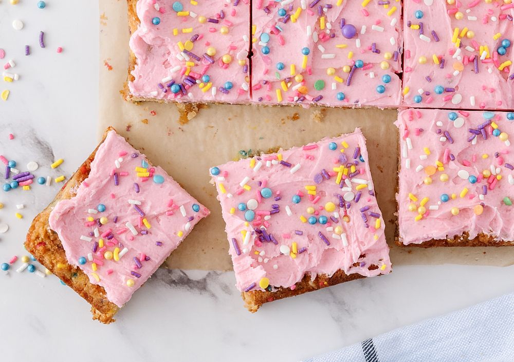 Pink frosted dessert bars topped with colorful sprinkles cut into squares.
