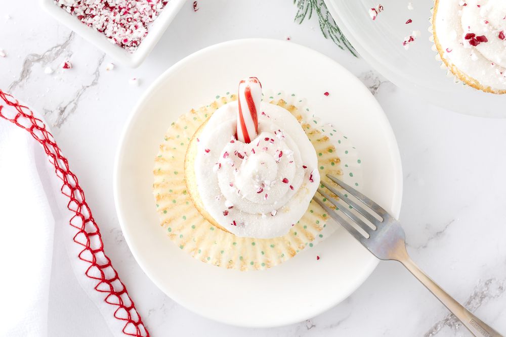 Peppermint cupcake with white frosting and candy cane garnish on a white plate.