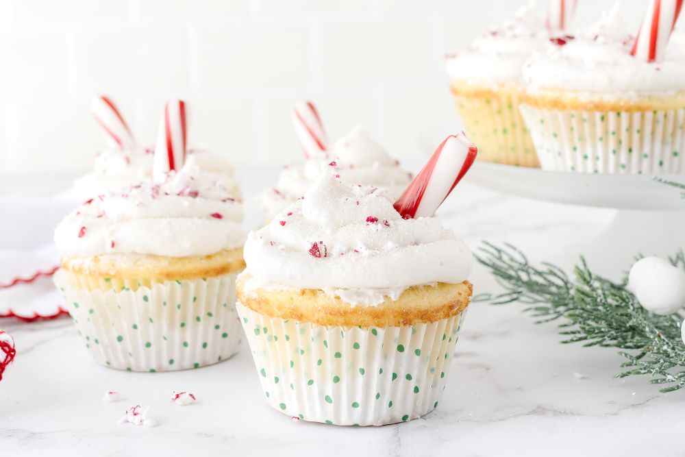 Holiday cupcakes decorated with peppermint sticks and crushed candy canes on a white surface.