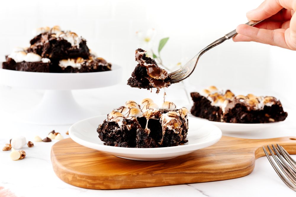 Chocolate brownies topped with toasted marshmallow being served on white plates.