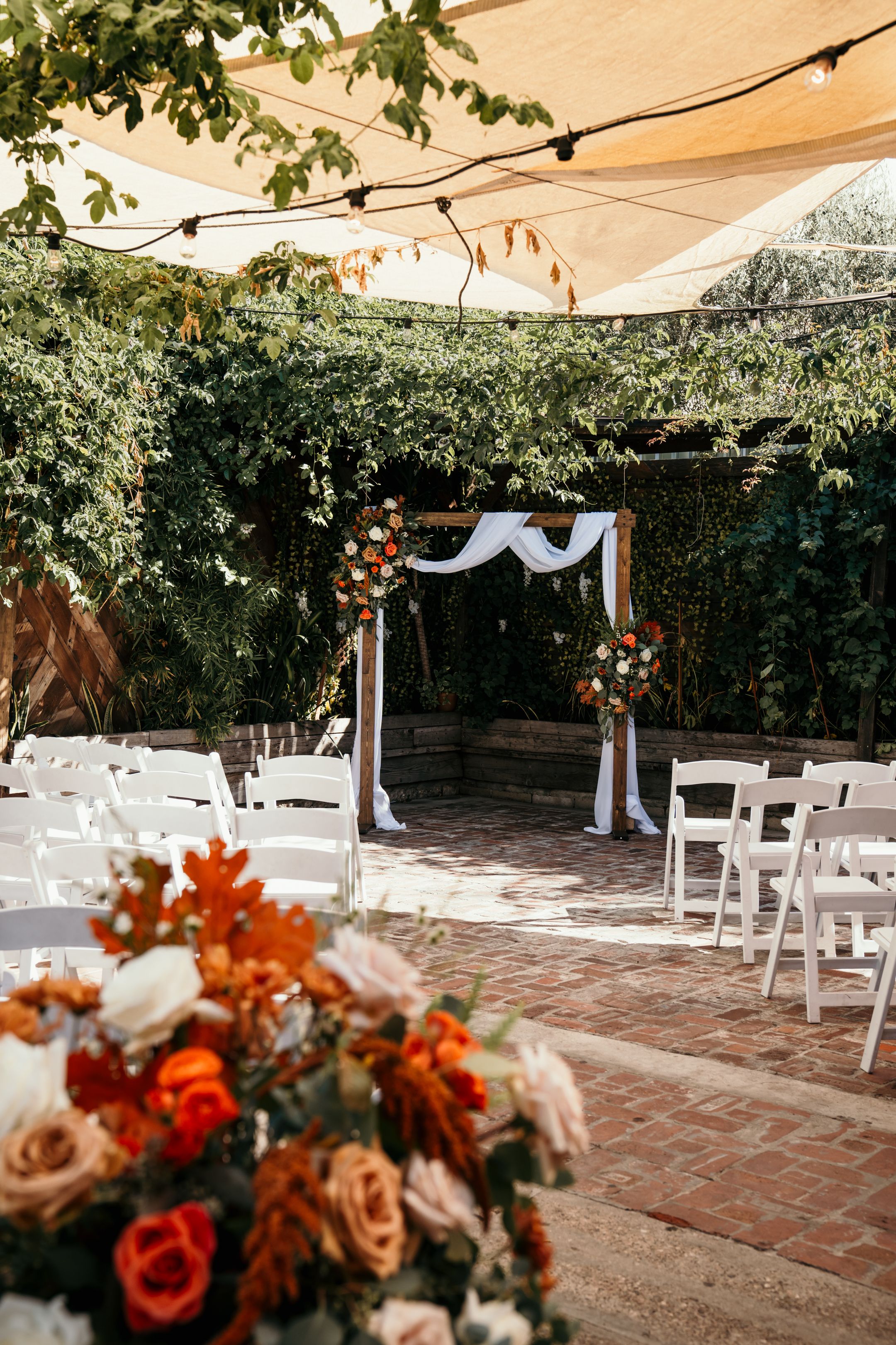 Outdoor wedding ceremony setup with white arch and orange floral arrangements.