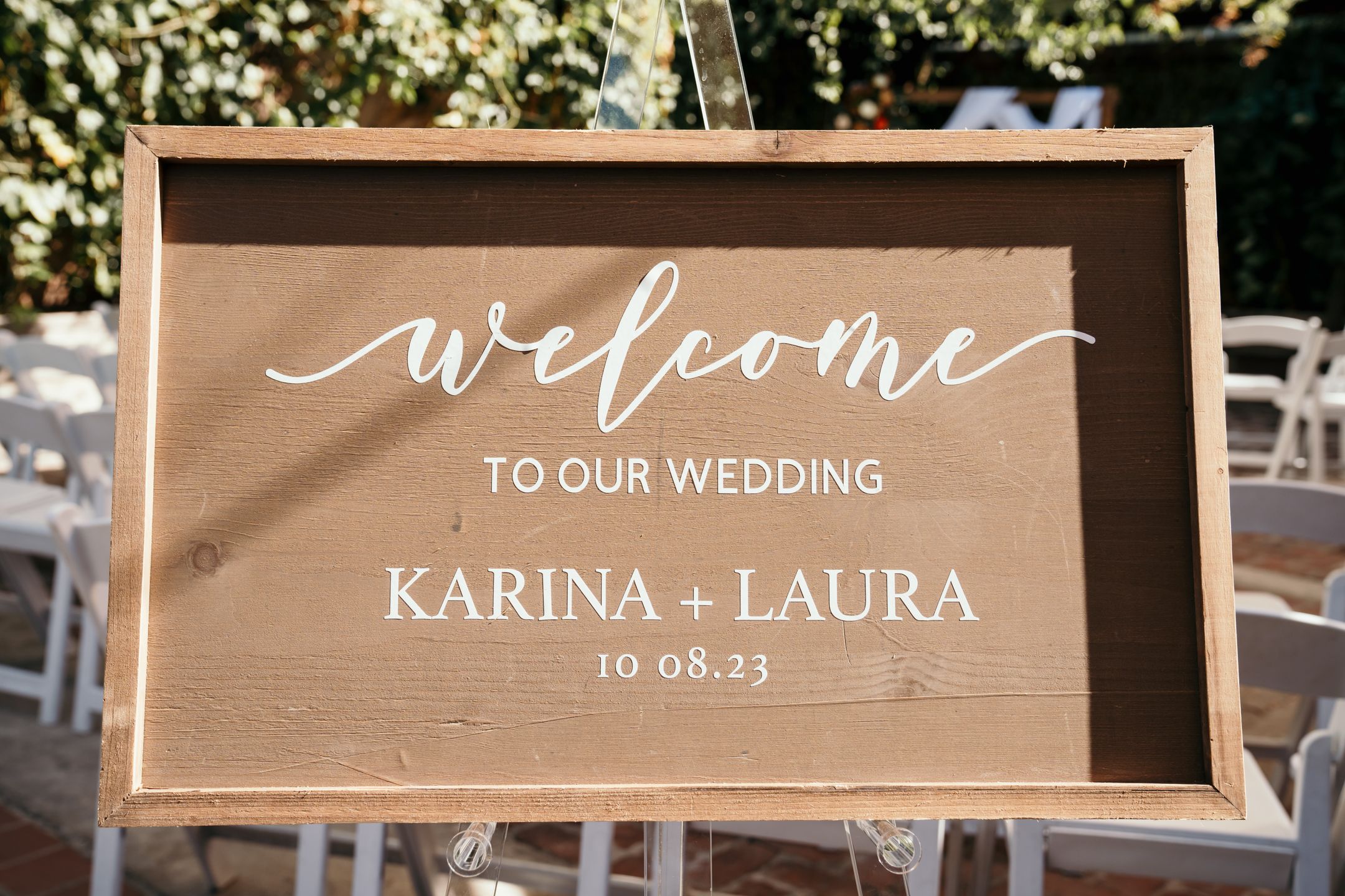 Wooden welcome sign for wedding with names and date in white calligraphy.