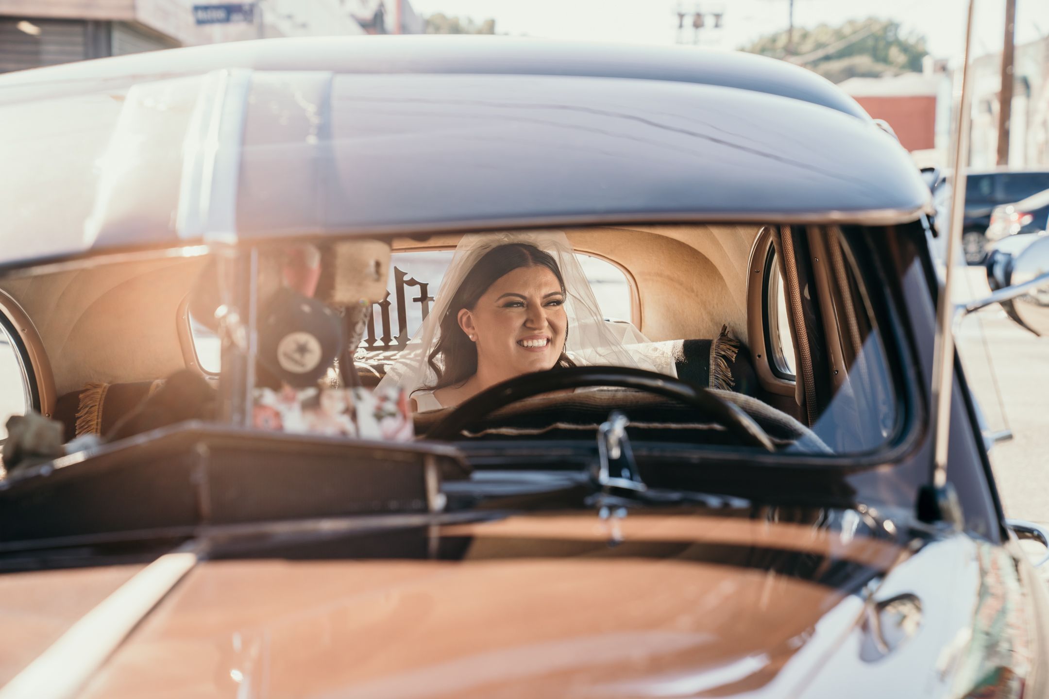 Person smiles while sitting in driver's seat of classic brown car.