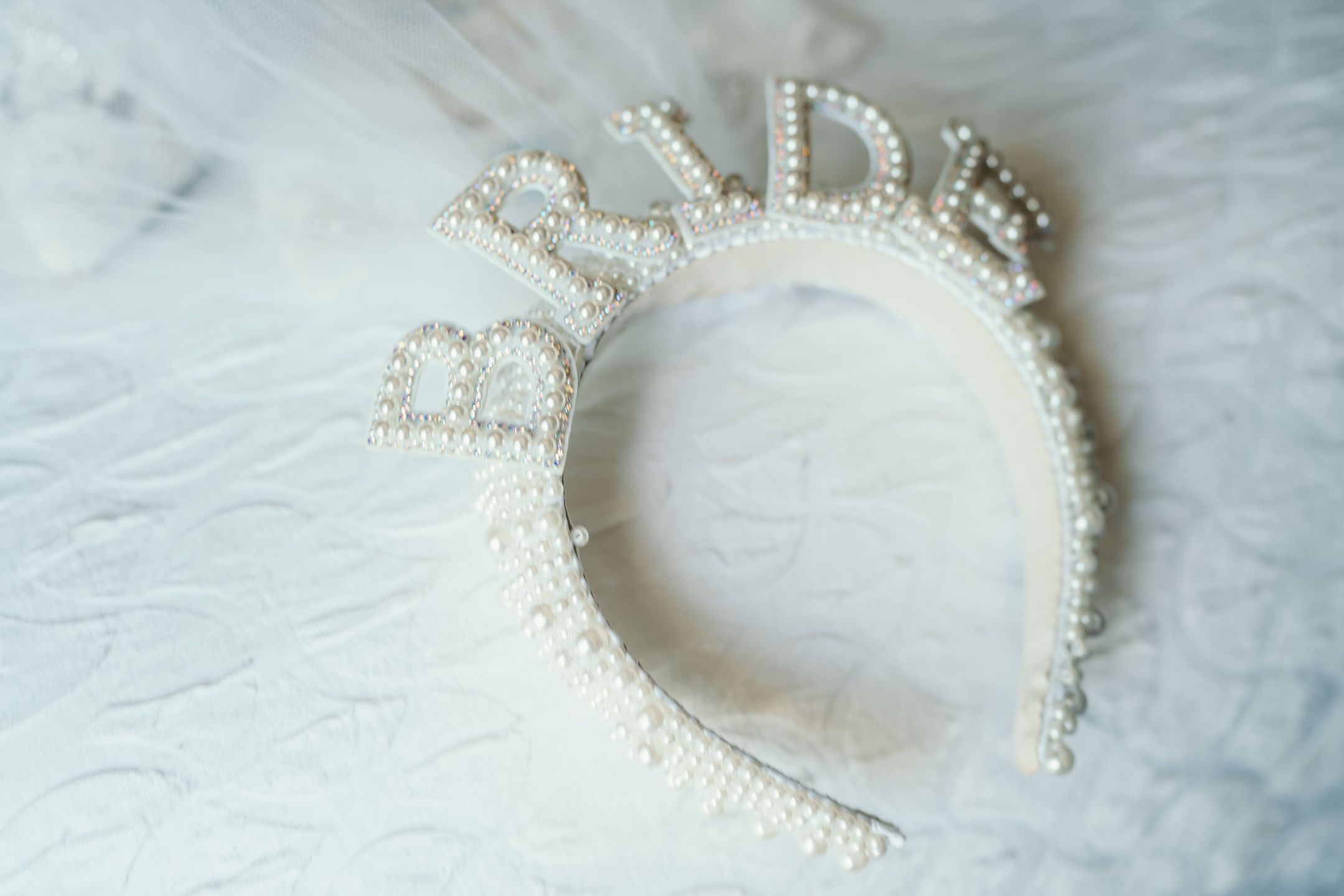 Pearl-encrusted 'BRIDE' headband on white fabric background.