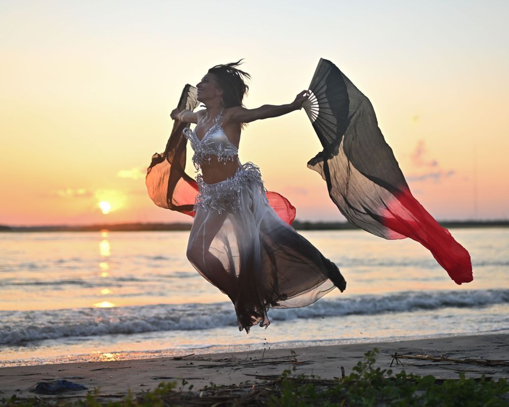 Dancer with billowing fabric performs dramatic jump on beach at sunset.