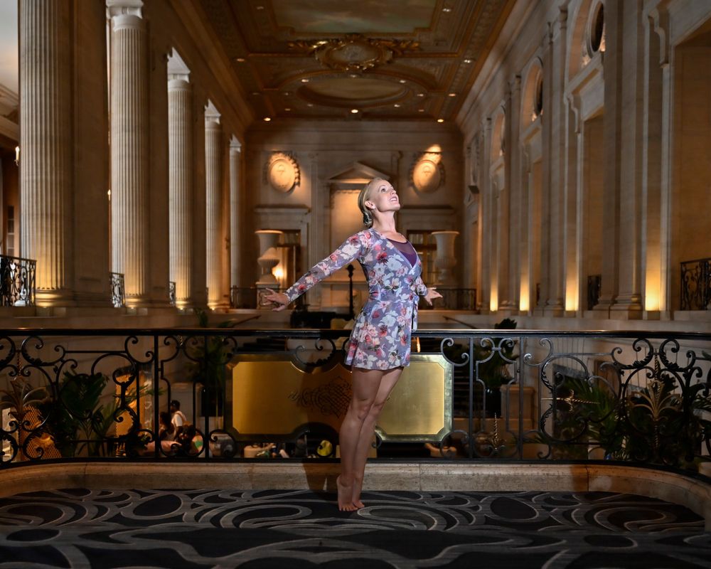 Dance performer strikes elegant pose in classical interior with marble columns and ornate details.