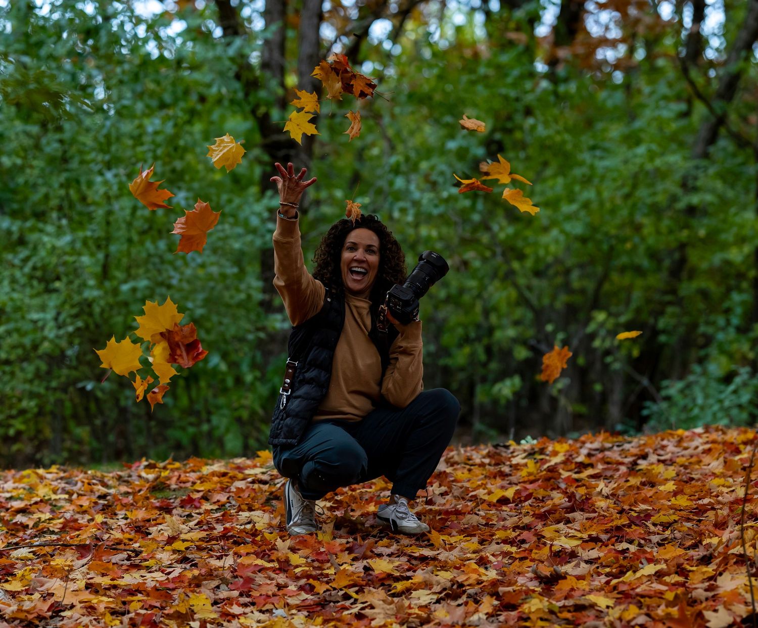 Photographer with curly hair holding camera equipment and having a sunflower tucked behind ear as decoration.