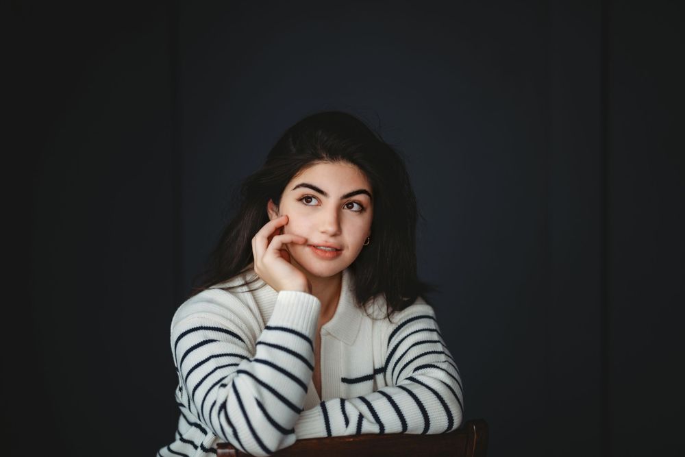 A moody portrait against dark background wearing a striped sweater in contemplative pose. Bellevue studio, WA