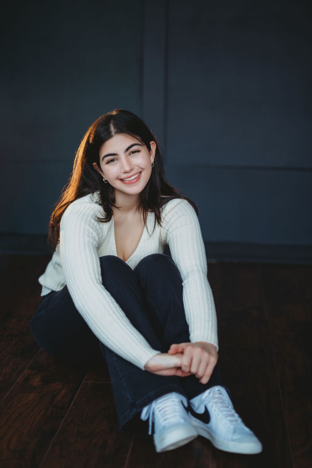 Casual indoor portrait on wooden floor wearing white sweater and dark pants. Bellevue studio, WA