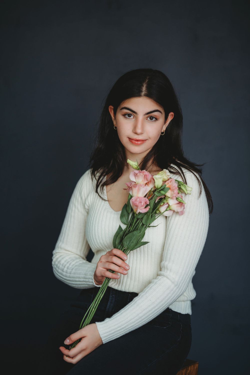 Studio portrait with pink roses against dark background wearing white ribbed sweater. Bellevue studio, WA