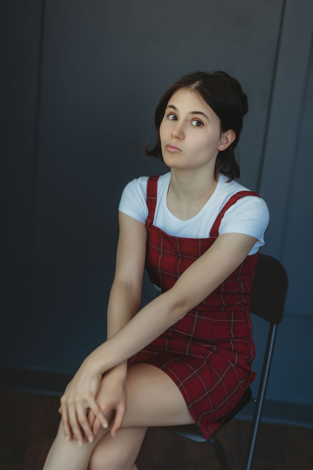 Portrait in red plaid pinafore dress seated against dark background. Bellevue studio, WA