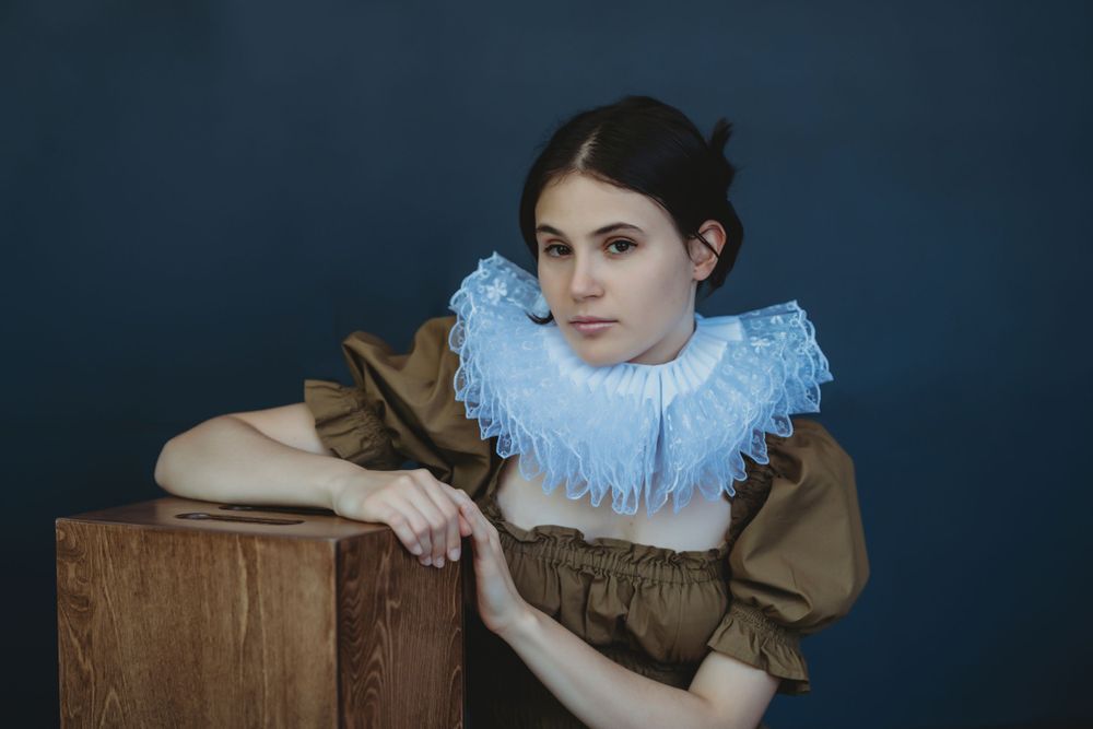 Portrait in vintage-style dress with ruffled collar against dark background. Bellevue studio, WA