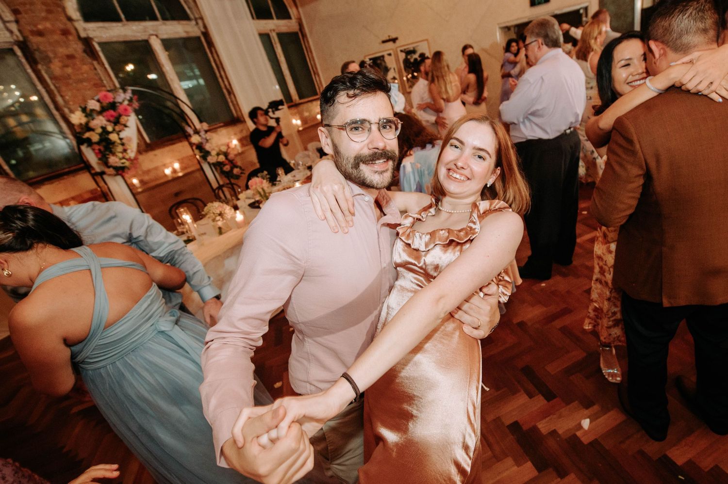 Wedding guests dancing and celebrating on a wooden dance floor at a reception.
