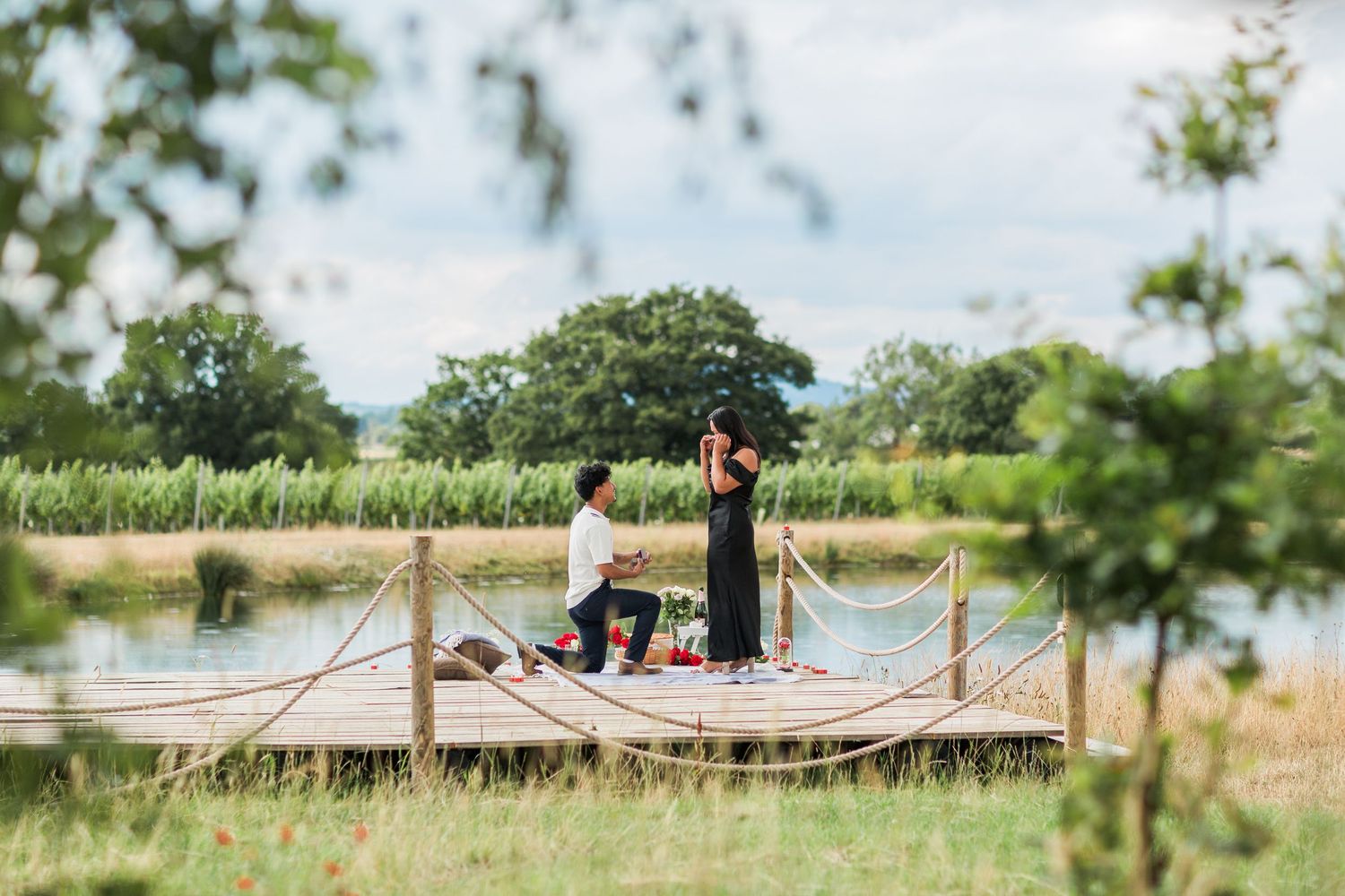 Romantic outdoor photo showing a man proposing to his partner by the side of a lake in The Cotswolds - Hayley Elizabeth Photography