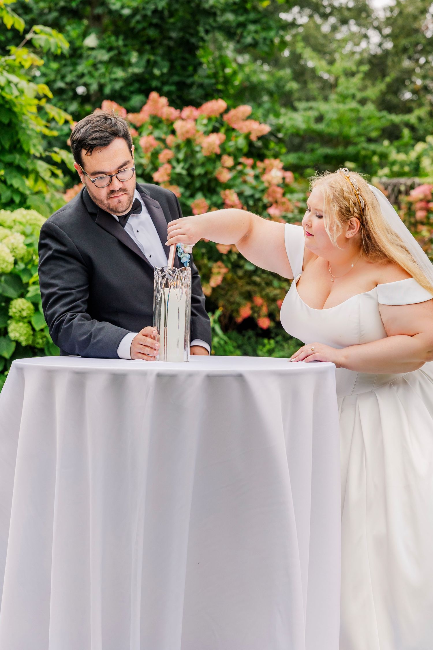 A couple in wedding attire shares a playful moment at their reception while drinking from champagne flutes.