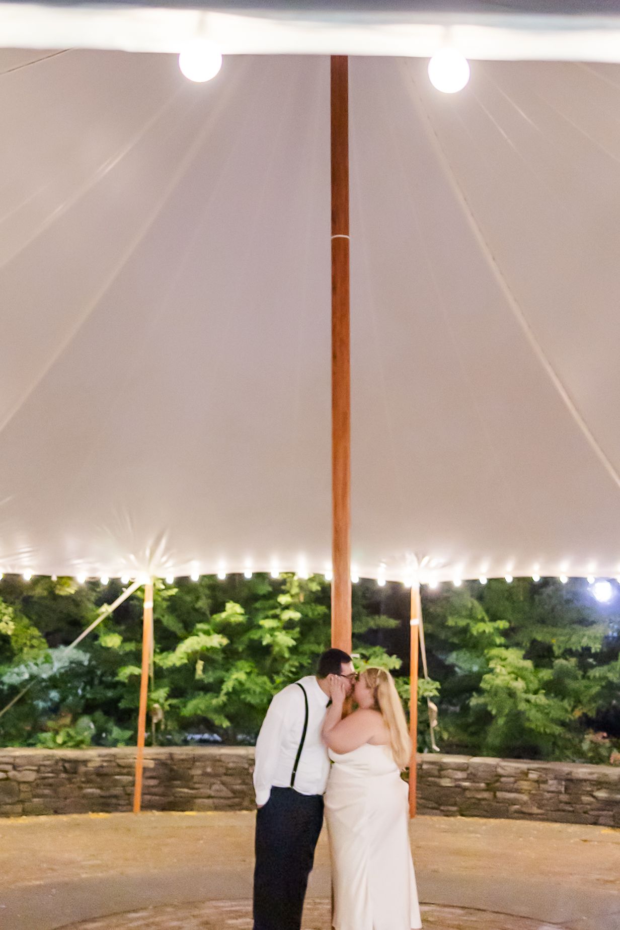A couple shares their first dance under a white tent on a circular patterned dance floor at dusk.