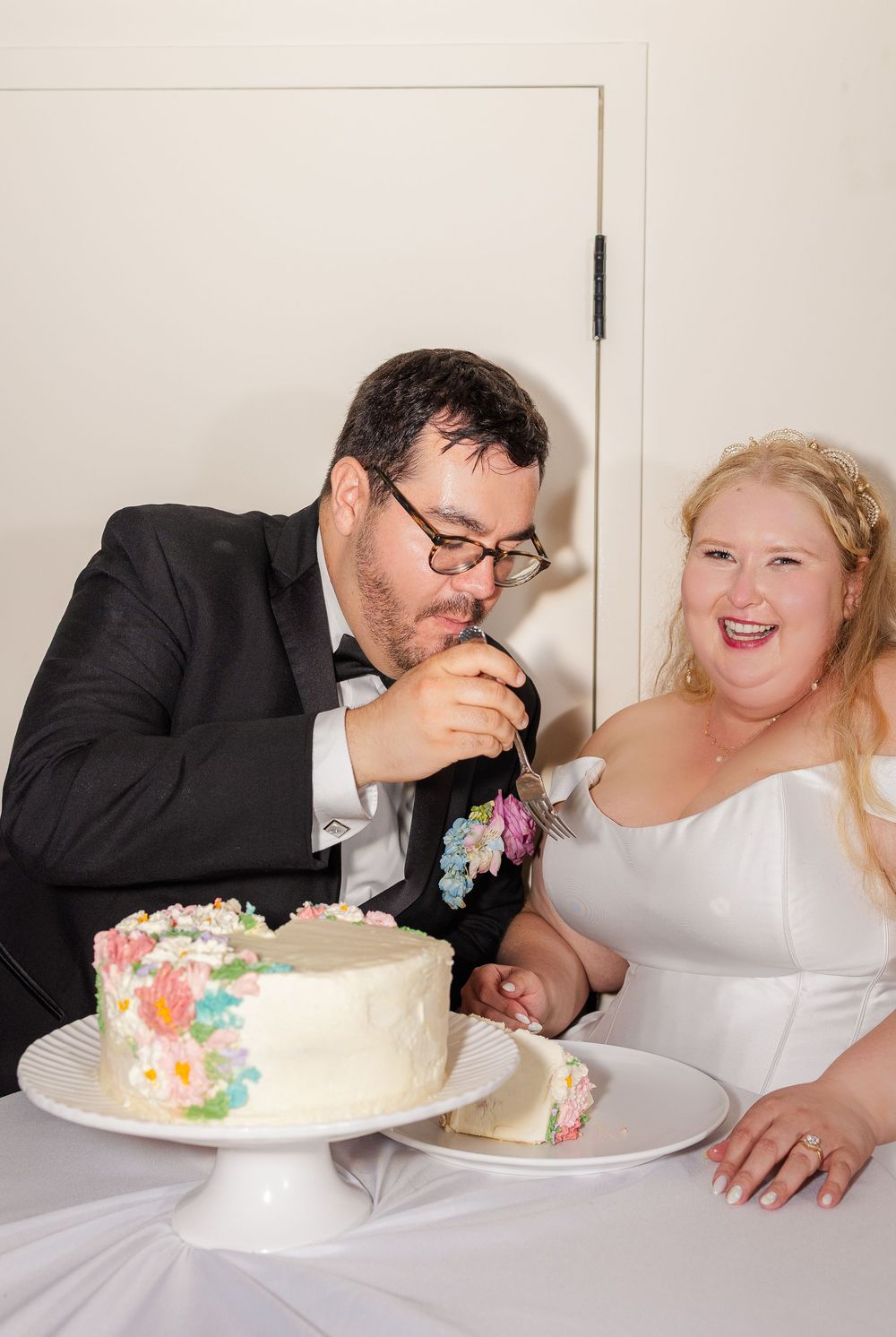 A couple shares a playful moment while eating their wedding cake at the reception.
