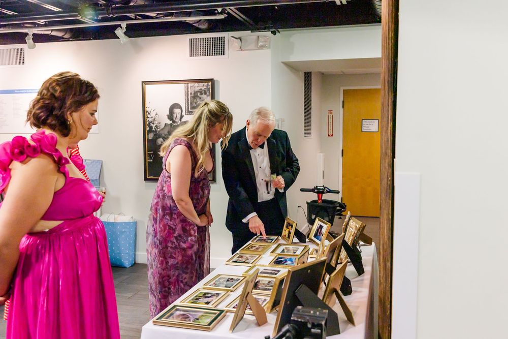 People viewing artwork displays in a gallery hallway with bright lighting and white walls.