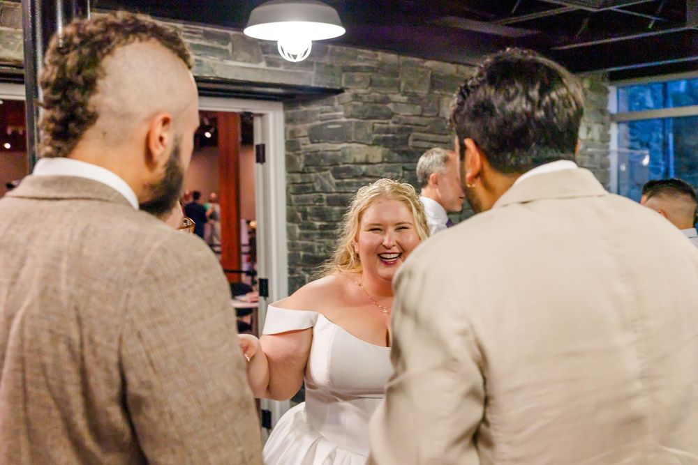 A joyful moment at a wedding reception with the bride in a white dress laughing with guests in a rustic venue.