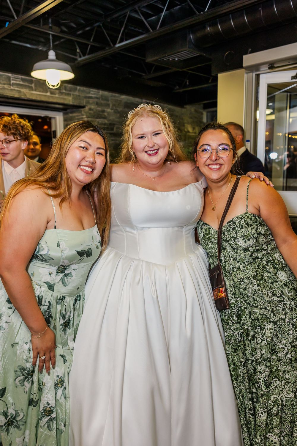 Wedding party wearing floral green and white dresses pose together indoors.