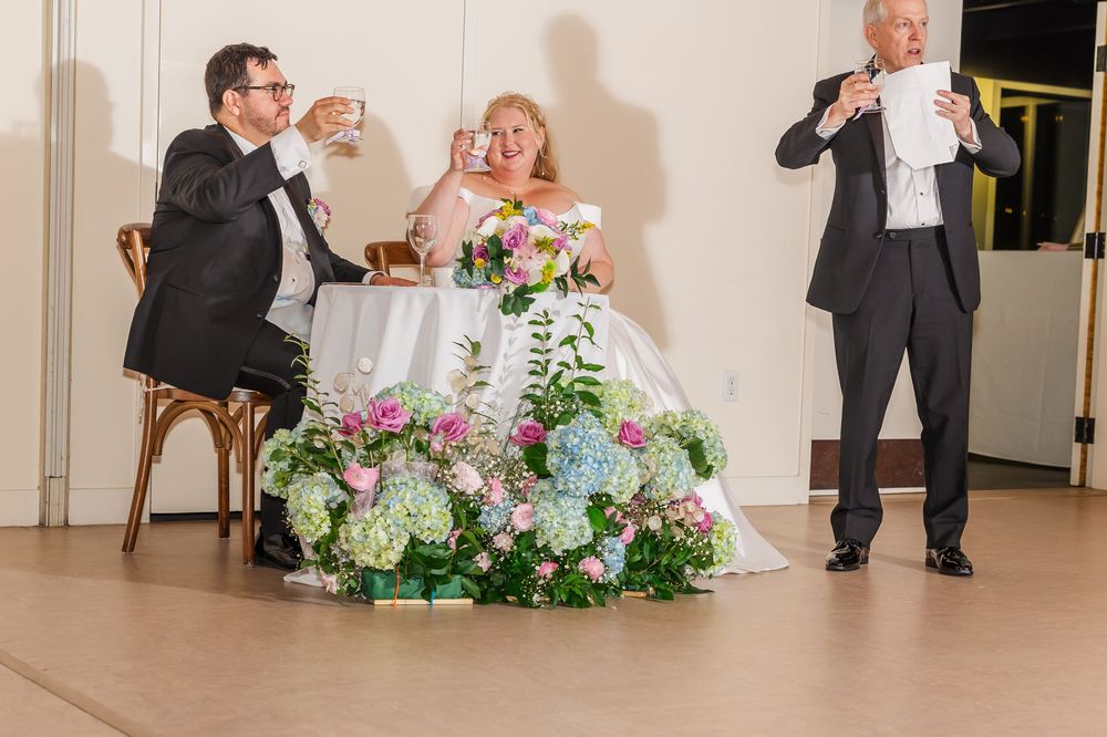 Wedding party dancing and celebrating during an elegant indoor reception with floral arrangements.