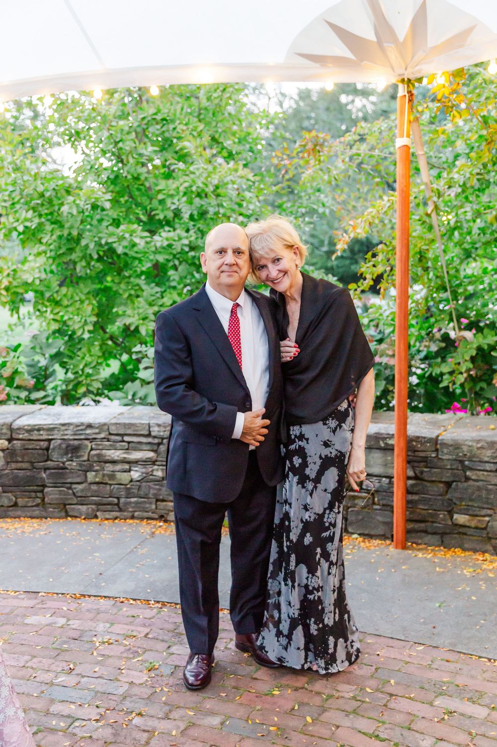 Couple shares intimate moments in an outdoor garden setting with stone walls and brick pathways.