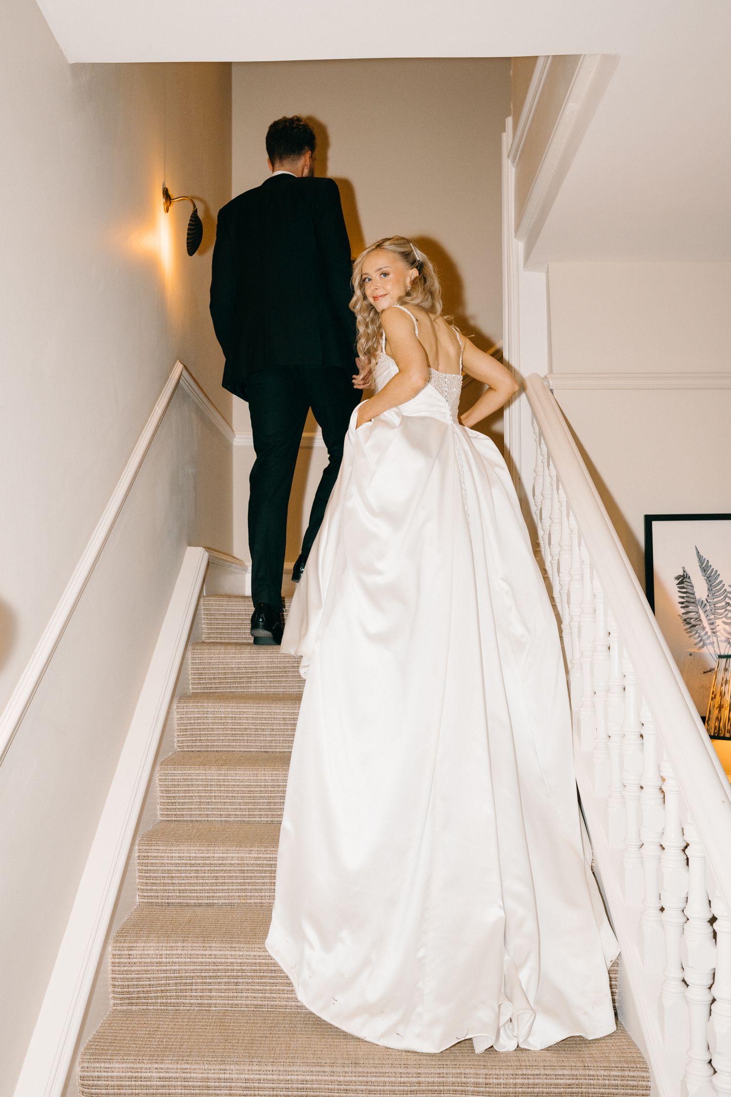 A couple in formal attire ascends a white staircase, with the bride's flowing white gown trailing behind them.