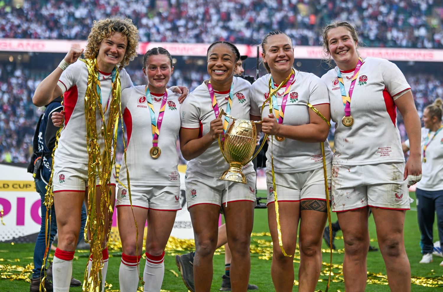 Rugby players celebrate with trophies and medals on field after championship victory at packed stadium.