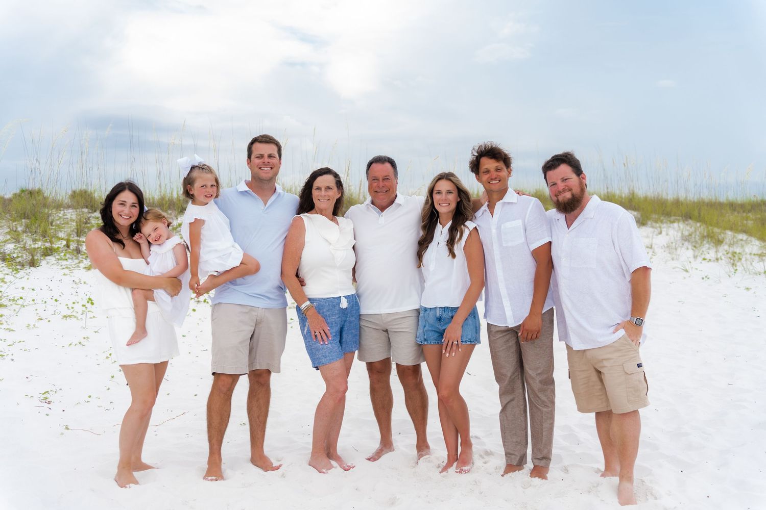 A group in white and khaki clothing poses together on a sunny white sand beach during a photo session.